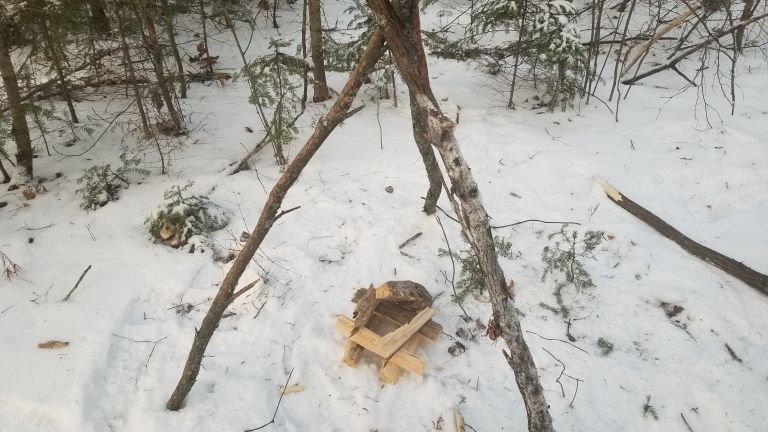 Homemade wood tripod grill setup. Kindling wood piled on snow.
