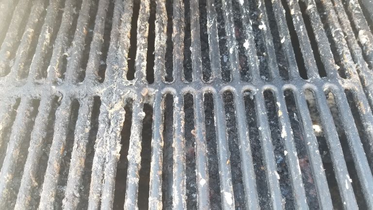 Cast iron grill grate that is very dirty. Stuck on food and barbecue sauce.