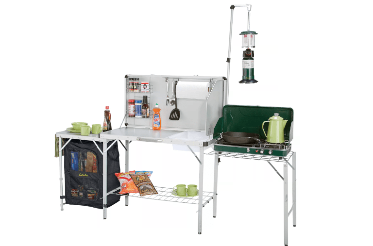 A foldable, portable camp kitchen with shelving, a grill station and hooks for storage.