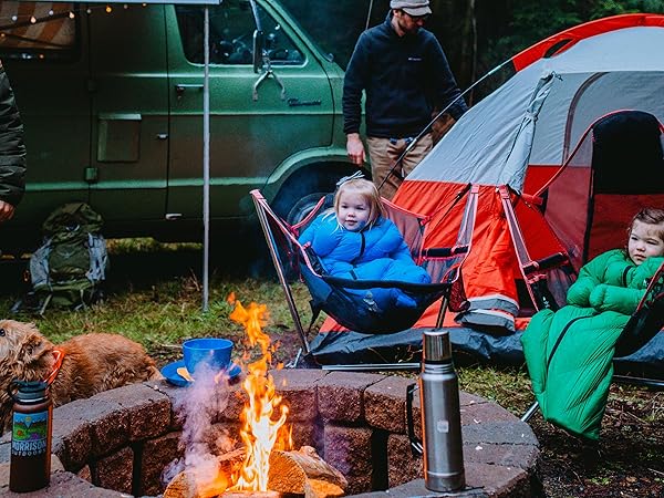 Kids are sitting by a campfire wrapped in sleeping bags