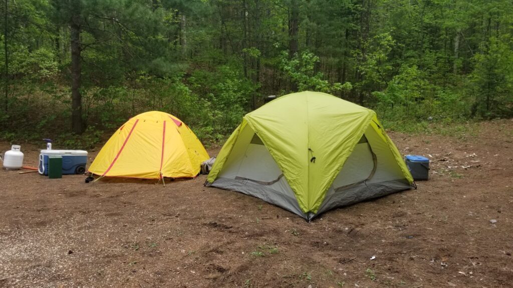 A yellow test and a green tent setup in the woods