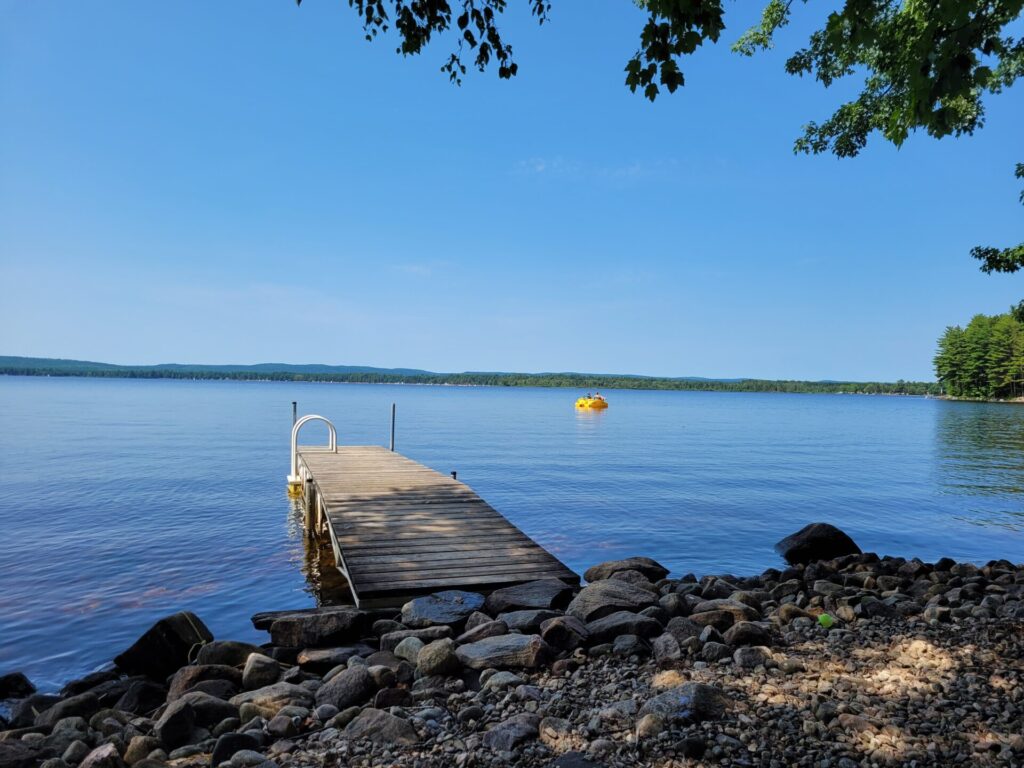 A wooden dock in a large lake on a clear sunny day. RV family camping by the lake.