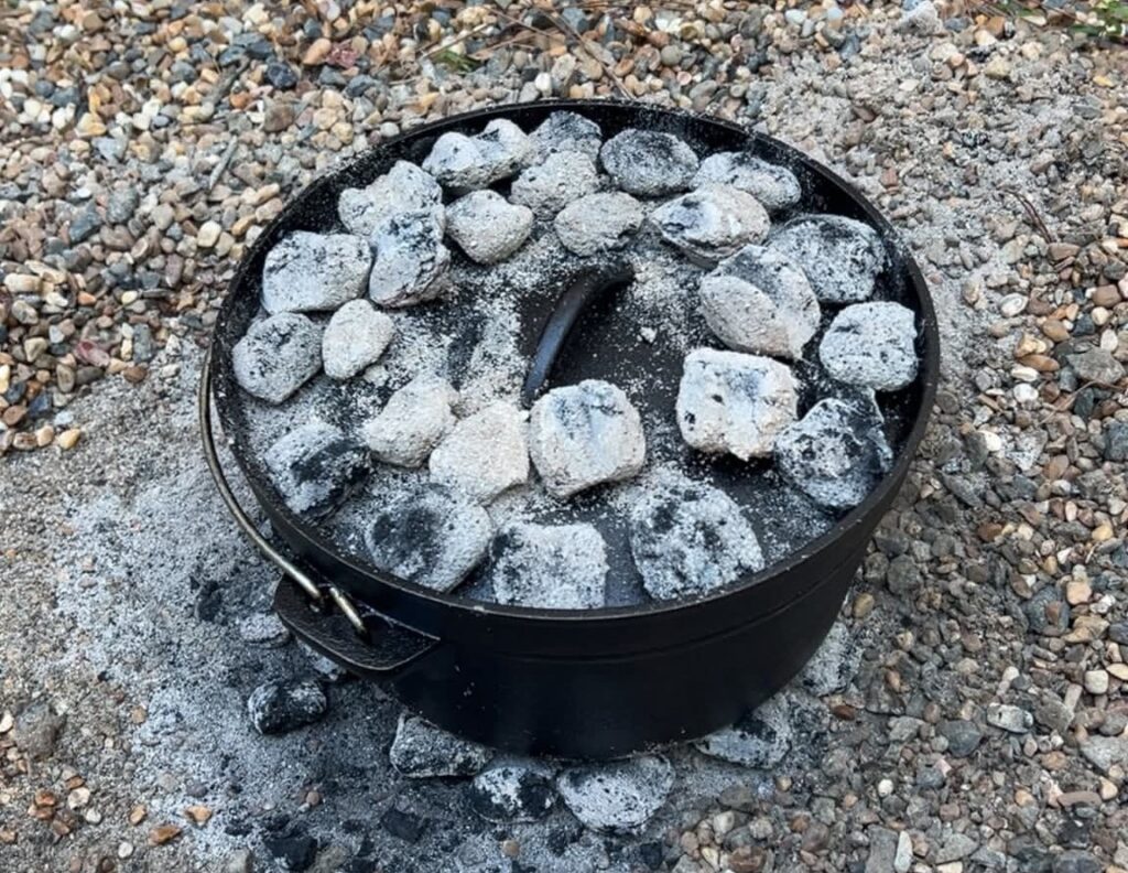A Dutch oven on the ground with coals on the lid